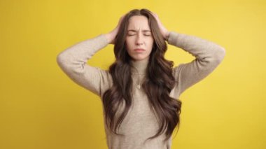 Genç bir kadın, baş ağrısına veya migrene işaret eden, elleriyle başını okşayarak, rahatsız edici bir görüntü sergiliyor.