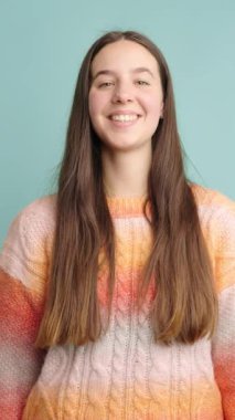 Neşeli bir kadın açık mavi arka planda farklı gülücükler ve ifadeler sergiliyor, sıcaklığı ve pozitifliği iletiyor.