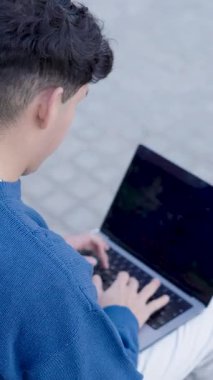 Genç adam dışarıda boş bir ekranla dizüstü bilgisayarında oturuyor ve daktilo yazıyor. Dikey görüntüler