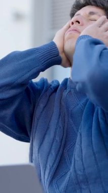 Dizüstü bilgisayarı üzerinde çalışırken stres ve hayal kırıklığı yaşayan genç bir adam yorgunluğunu ve yorgunluğunu ifade ediyor. Dikey görüntüler