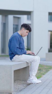Kampüs bankında oturan, akademik proje üzerinde çalışırken modern binanın yakınında dizüstü bilgisayar üzerinde çalışan bir üniversite öğrencisi. Dikey görüntüler