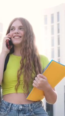 Üniversite öğrencisi elinde defterlerle güneşli bir günde sınıfa yürürken hoş bir telefon konuşması yapmaktan hoşlanıyor. Dikey görüntüler