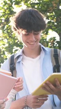 Üniversite öğrencileri güneşli bir günde kampüste tartışırken açık havada dijital bir tablet ekranı paylaşıyorlar. Dikey görüntüler