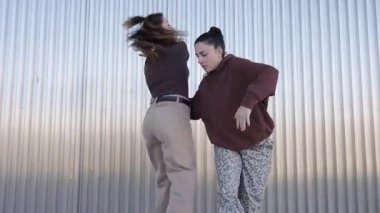 İki genç dansçı, kıvrık demir bir duvarın önünde modern bir dans koreografisi çalışırlar.