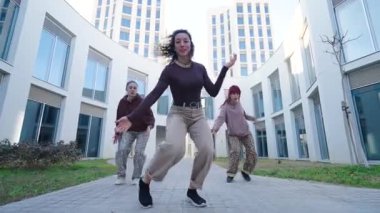 Yetenekli dans ekibi canlı şehir manzarasında yüksek enerji ve sanatsal ifade ile senkronize hip hop hareketleri yapıyor, takım çalışmasını ve tutkusunu vurguluyor.