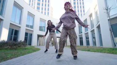 İki kadın dansçı modern bir binanın önünde koreografik dans gösterisi yapıyorlar.