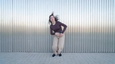 Dinamik dansçı kıvrımlı metal arka planına karşı serbest dans ederek güçlü koreografi ve vücut dili ile kentsel enerjiyi ifade ediyor.