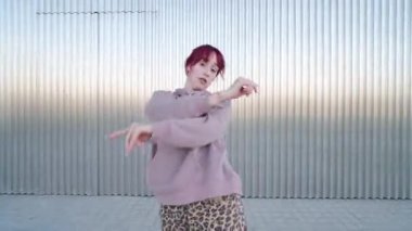 Kızıl saçlı bayan dansçı dinamik kent dansı yapıyor, metalik endüstriyel arka planda tutkulu hareketlerle sanatsal yaratıcılığını ifade ediyor.