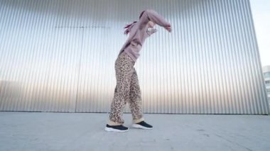 Kızıl saçlı dansçı metalik arka planda enerjik bir ifadeyle dinamik sokak dansı hareketleri yapıyor.