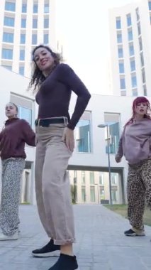 Dinamik bayan dansçılar, şehir mimarisi arka planına karşı senkronize hip hop koreografisi uyguluyor, güneşli açık hava gösterilerinde çağdaş hareketleri ve takım enerjisini sergiliyorlar.