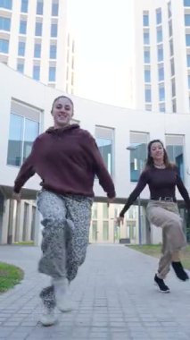 İki genç kadın, şehir ortamında hareketlerini dinamik ve senkronize bir şekilde sergiliyorlar.