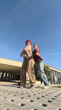 İki genç dansçı, üniversite kampüsündeki dairesel taş bir platformda modern bir koreografi sergiliyor.