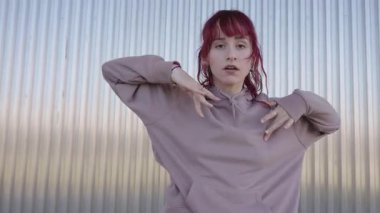 Profesyonel kızıl saçlı dansçı, çağdaş koreografiyi yürütüyor, Stark metal duvar arka planına karşı dinamik vücut hareketleri yapıyor.