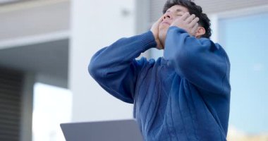 Dizüstü bilgisayarı üzerinde çalışırken stres ve hayal kırıklığı yaşayan genç bir adam yorgunluğunu ve yorgunluğunu ifade ediyor.