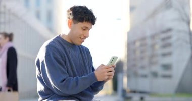 Genç erkek akıllı telefonuyla neşeyle meşgul olurken şehir caddesinde dikiliyor, dijital iletişimin ve kablosuz bağlantının keyfini çıkarıyor.