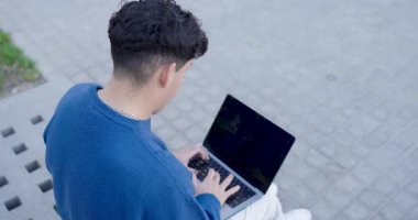 Dışarıda dizüstü bilgisayarda çalışan genç adam, doğal şehir ortamında odaklanmış dijital verimliliğin birden fazla perspektifini yakalıyor.