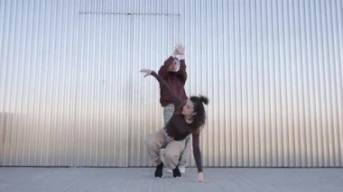 Senkronize modern dans koreografisini uygulayan kadın sanatçılar, dinamik enerji ve akışkan hareketle kentsel metalik duvar zeminine karşı sanatsal yaratıcılıklarını ifade ediyorlar.