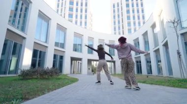 İki kadın dansçı, modern mimarinin arka planına karşı enerjik hareketlerini sergilemek için açık havada koreografik bir dans sergiliyorlar.