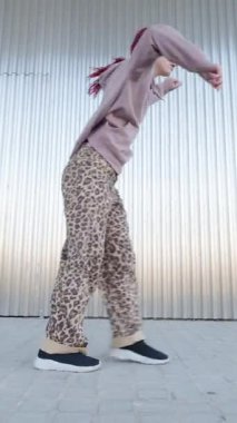 Günlük kıyafetlerle kızıl saçlı dansçı metalik arka planda sokak dansı yapıyor.