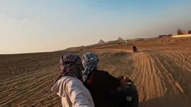 Maceraperest turistler gün batımında ikonik giza piramitlerini çevreleyen altın çölde dörtlü bisiklete biniyorlar.