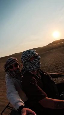 Maceraperest turistler altın çöl kum tepelerinde bisiklet sürüyorlar. Egzotik ortadoğu manzarasında heyecan verici günbatımı anları yaşıyorlar.