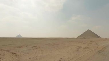 Taramalı panoramik manzara, tarihi Dahshur mezarlığındaki tozlu çöl manzarasından yükselen bükülmüş ve siyah piramitlerin katıksız siluetlerini ortaya çıkarıyor. Eski Mısır mimarisinin ihtişamını vurguluyor