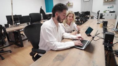 İki genç profesyonel, bir erkek ve bir kadın, modern bir ofiste dizüstü bilgisayarda birlikte çalışıyorlar, takım çalışması ve işbirliği gösteriyorlar.