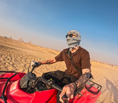 Mısır çölünde Giza piramit kompleksini keşfeden keffiyeh giyen ve güneş gözlüğü takan bir turist.
