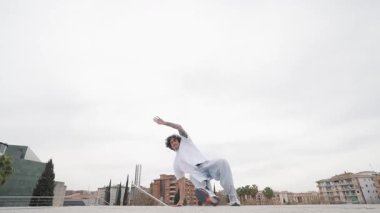 Şehir çatısı üzerinde akrobatik hareketler yapan dinamik break dansçı, şehir planına karşı yoğun beceri ve yaratıcı hareket sergiliyor.