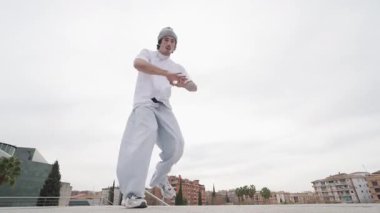 Genç erkek sanatçının dinamik dans performansı şehir manzarasında enerjik hip hop stili ifade ederek serbest stil hareketini ve yaratıcı ritmi gösteriyor.