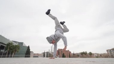 Becerikli break dansçı, dayanıklılık, denge ve dinamik kentsel dans tekniğini göstererek cesur şehir manzarasına karşı gösteri yapıyor.