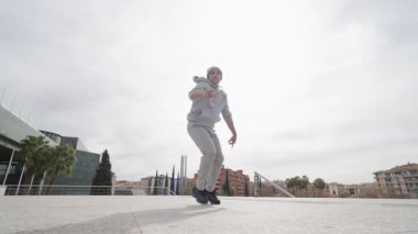 Genç break dansçı gündüz antrenmanı sırasında atletik enerji ve şehir stiliyle dinamik akrobatik sokak hareketleri yapıyor.