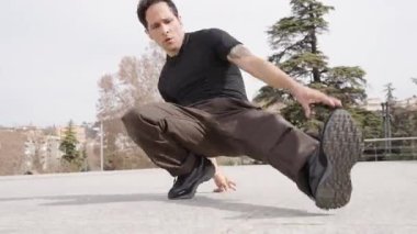 Yetenekli break dansçı, donma hareketleri sergiliyor. Şehir parkı ortamında güç, denge ve kontrol gösteriyor.