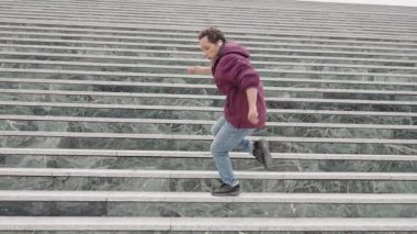 Şehir basamaklarında dinamik koreografi pratiği yapan genç bir dansçı, kulaklıkla ritmik hareket eden, kişisel tarzını ve müziğe olan tutkusunu ifade eden
