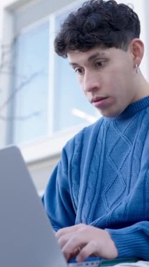 Genç öğrenci dışarıda dizüstü bilgisayarı üzerinde çalışırken şaşkınlıktan hayal kırıklığına ve öfkeye kadar çeşitli ifadeler sergiliyor. Dikey görüntüler