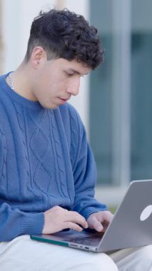 Laptop üzerinde çalışırken dikkatlice odaklanan genç profesyonel, dışarıdaki ortamlarda modern uzaktan öğrenme ve dijital bağlantı gösteriyor. Dikey görüntüler