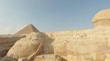 Khafre Piramidi 'ni koruyan görkemli sfenks, antik Mısır' ın tarihi Giza Çölü manzarasında açık mavi gökyüzüne karşı dimdik ayakta duruyor.