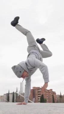 Enerjik break dansçı bir amuda kalkıyor, güç ve denge gösterisi kentsel bir zemine karşı