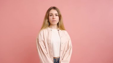 Kendine güvenen bir vücut dili sergileyen genç bir kadın model. Pastel pembe stüdyo arka planına karşı şık bir kıyafetle poz veriyor. Değişik dışavurumlar sergiliyor.