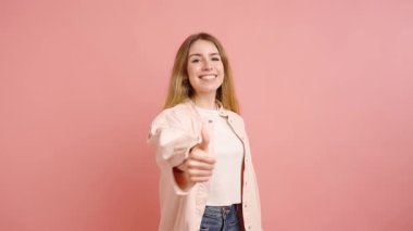 Mutlu genç bir kadın pembe arka planda izole edilmiş onay, anlaşma ya da destek jestleri gösteriyor.