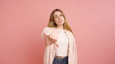 Genç bir kadın güçlü bir anlaşmazlığı klasik baş parmaklarıyla ifade ederek negatif duygularını canlı pembe stüdyo geçmişine aktarıyor.