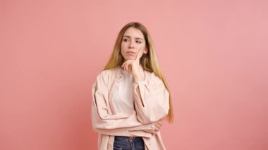 Farklı duyguları ifade eden genç bir kadının stüdyodaki görüntüsü. Kuşkudan tatmin olmaya, pembe bir arka planda izole edilmiş.
