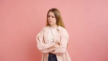 Kollarını çapraz yapmış, pembe bir arka planda izole edilmiş çeşitli yüz ifadeleri gösteren sıradan bir genç kadın.