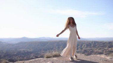 Kadın, güneş ışığını kucaklayarak, manzaralı bir dağ manzarasında zarif bir şekilde dans ediyor. Doğada özgürlüğün ve sevincin ifadesi