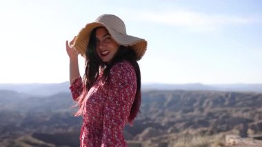 Şapkalı bir kadın özgürlüğünü ve doğayı kutlayan güzel bir dağlık alanda sevinçle döner ve kollarını uzatır.