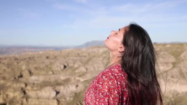 Dişi gezgin, çöl zirvesinde duruyor, derin derin nefes alıyor, rüzgarı deneyimliyor ve derin özgürlük ve iç huzur hissiyle el değmemiş manzarayı kucaklıyor.