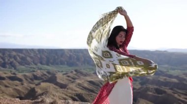 Altın gün batımında dramatik çöl kanyonu manzarasına doğru ilerlerken kırmızı elbise giyen zarif bayan dansçı.