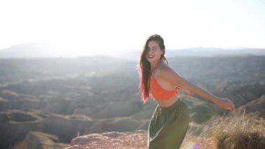 Şık manken, altın saat günbatımında dağın zirvesinde özgürce dans ediyor. Sersemletici manzaraya karşı macera ve kişisel özgürlüğün vücut bulmuş hâli.