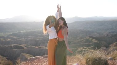 Manzaralı bir dağ manzarasının keyfini çıkaran iki kadın akıllı telefonuyla eğlenceli anları yakalıyor. Günışığı arkaplanı sevinçlerini ve bağlantılarını vurguluyor