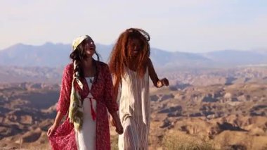 Tarz sahibi bayan arkadaşlar güvenli bir şekilde çöl manzarasında yürüyor, rüzgarlı saçlar ve canlı moda ile tasasız anın tadını çıkarıyorlar.